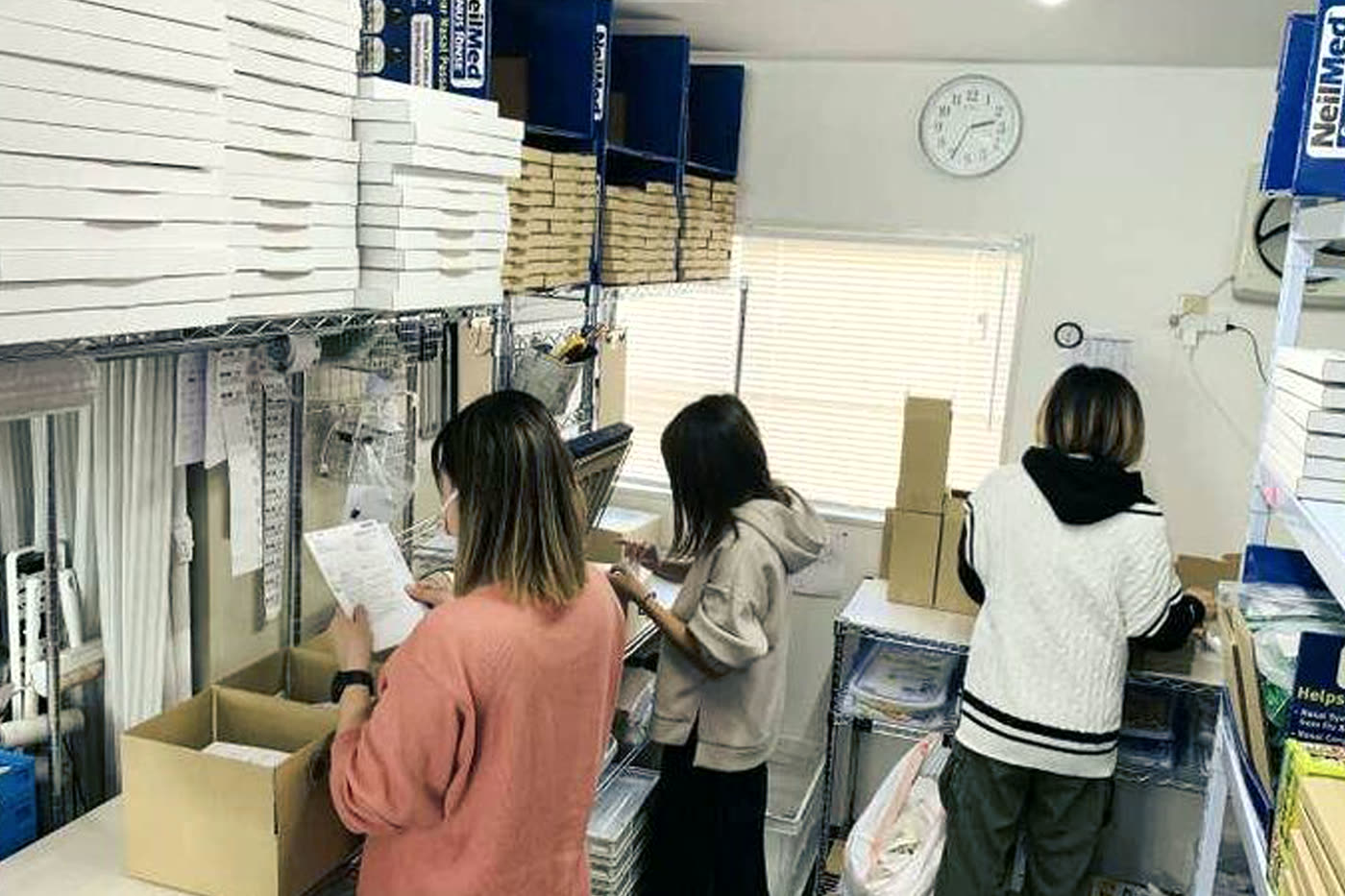 梱包資材の棚の前で3人のスタッフが同時に作業している後ろ姿